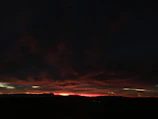 A dark, smoky landscape with faint red and gold light breaking through heavy clouds.