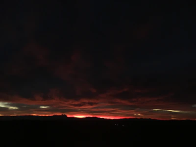 A dark, smoky landscape with faint red and gold light breaking through heavy clouds.