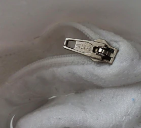 An ergonomic button hook and zipper pull tool displayed on a soft fabric background.