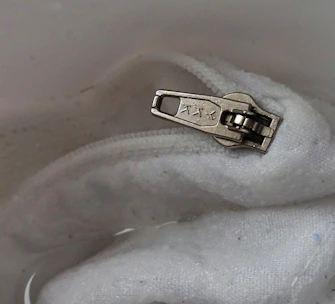 An ergonomic button hook and zipper pull tool displayed on a soft fabric background.
