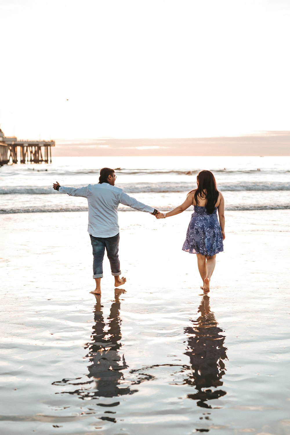 man and woman holding hands while walking on seashore