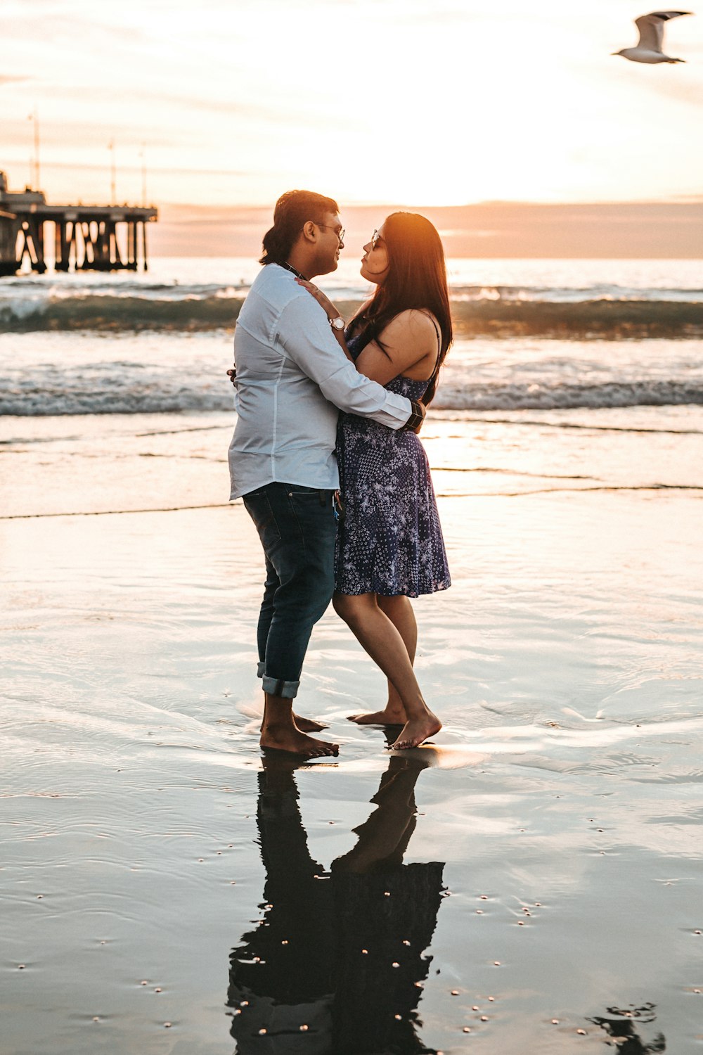 man in white shirt beside woman in dress standing on beach