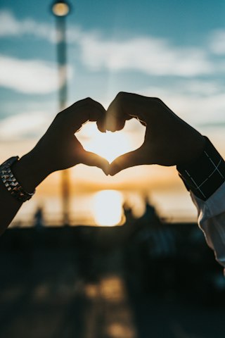 Deux mains formant un cœur au coucher du soleil, illustrant le couple marié sous un régime de communauté