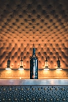 A bottle of wine is placed on a metallic counter adorned with raised circular patterns. The background features a tufted, upholstered surface with warm lighting, giving a luxurious and elegant atmosphere.