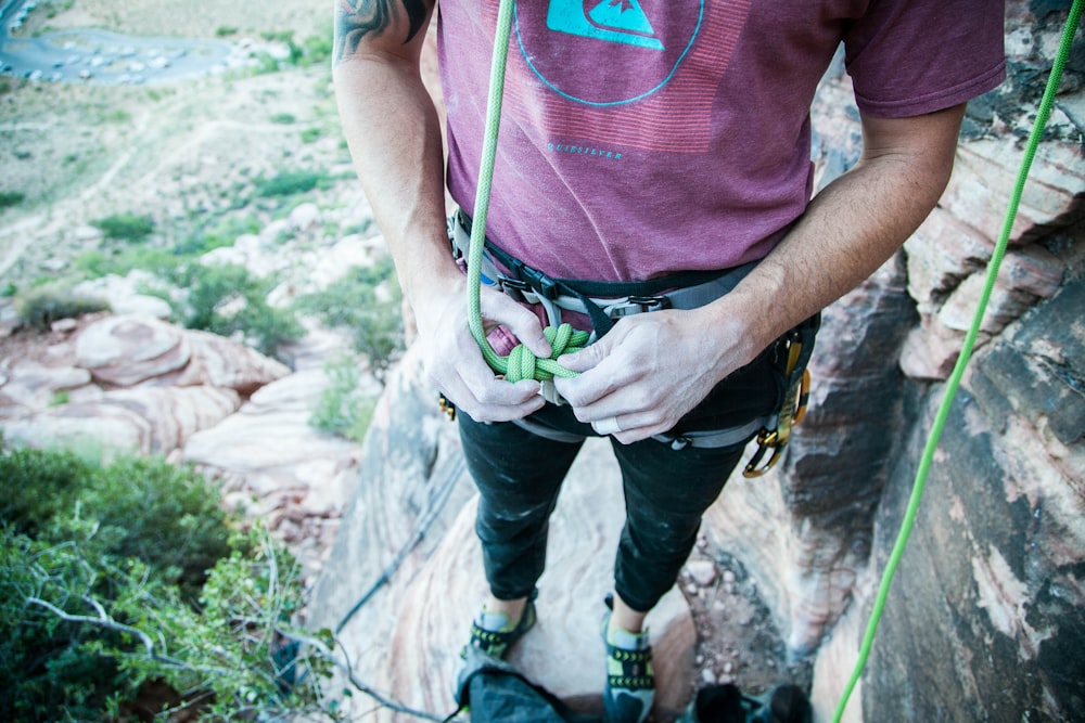 person holding green cable standing on mountain cliff