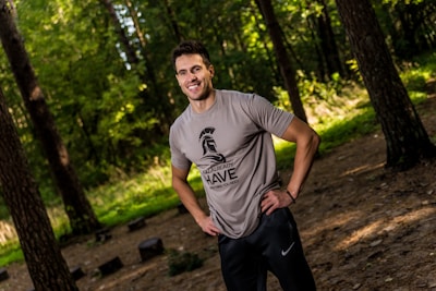 A smiling man wearing a fun, godly-themed t-shirt standing outdoors surrounded by nature.