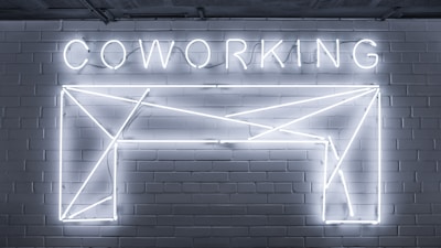 Neon lights form the word 'COWORKING' and an abstract geometric shape mounted on a brick wall. The design is sleek and modern, with a minimalistic style.