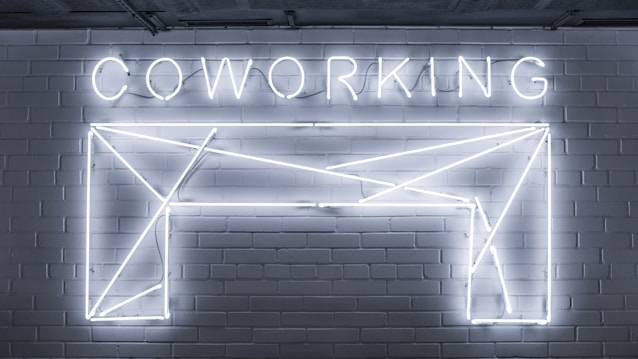 Neon lights form the word 'COWORKING' and an abstract geometric shape mounted on a brick wall. The design is sleek and modern, with a minimalistic style.