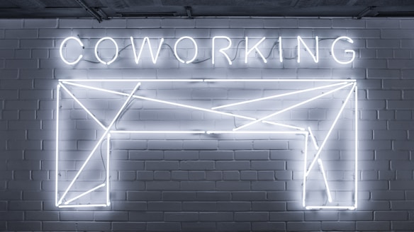 Neon lights form the word 'COWORKING' and an abstract geometric shape mounted on a brick wall. The design is sleek and modern, with a minimalistic style.