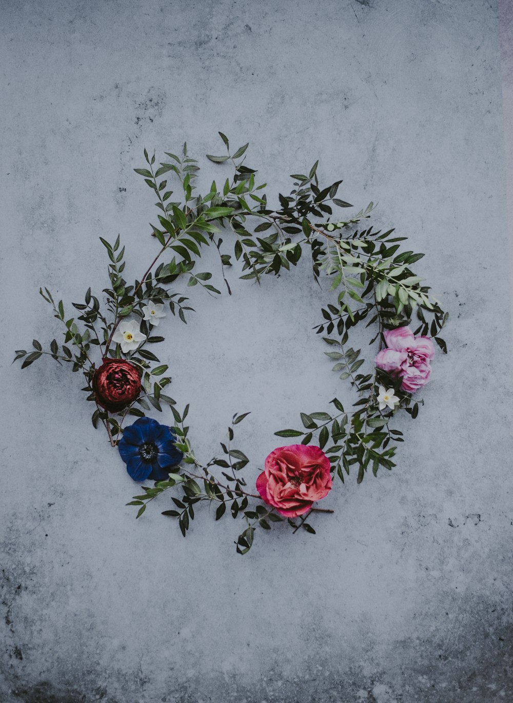 Corona de flores rojas, azules y blancas sobre hormigón blanco