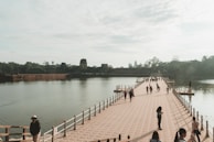 Pilgrims crossing a wooden bridge over a flowing river, framed by lush greenery and temple silhouettes.