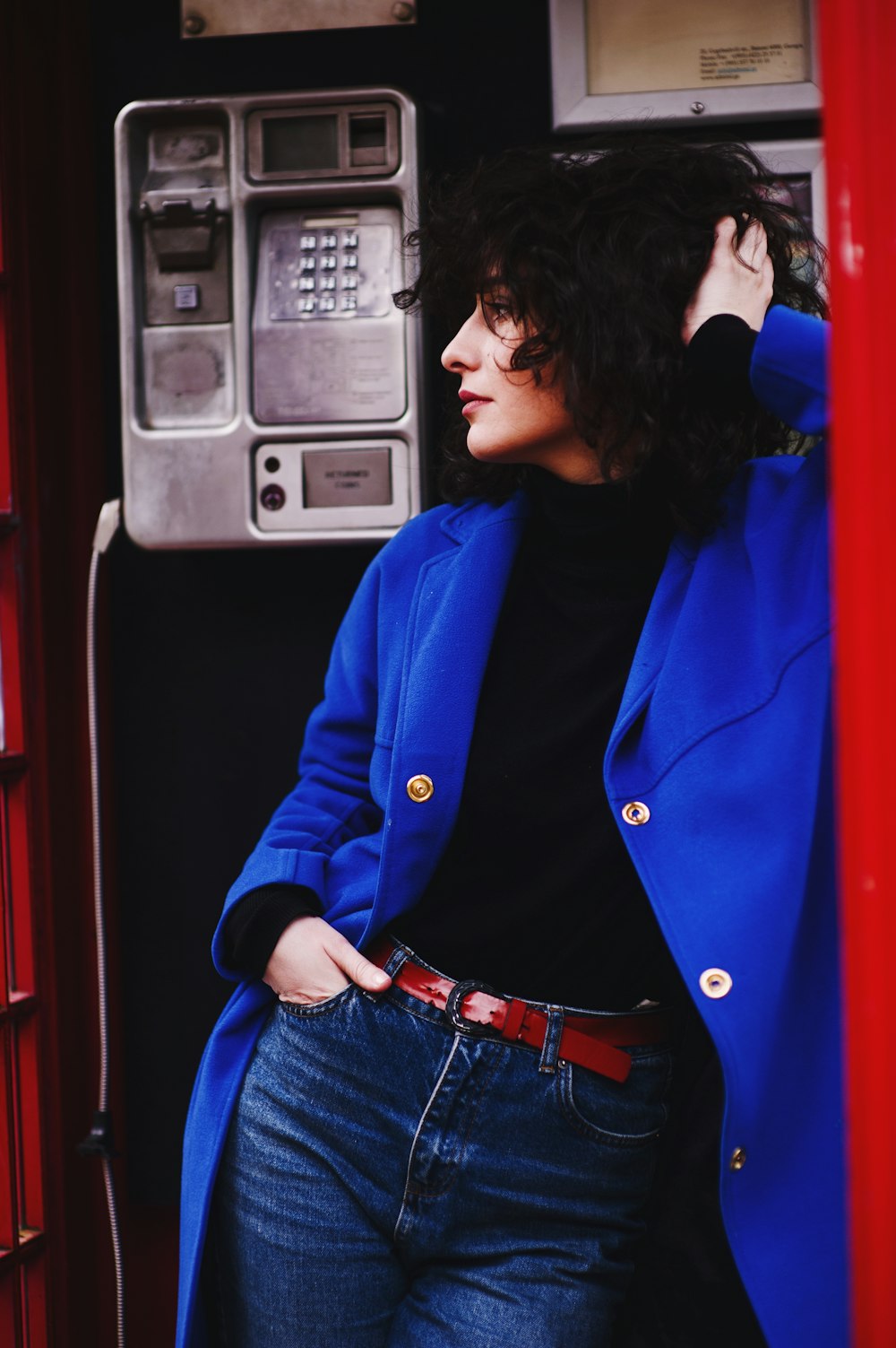 woman leaning on telephone booth wearing blue leather coat