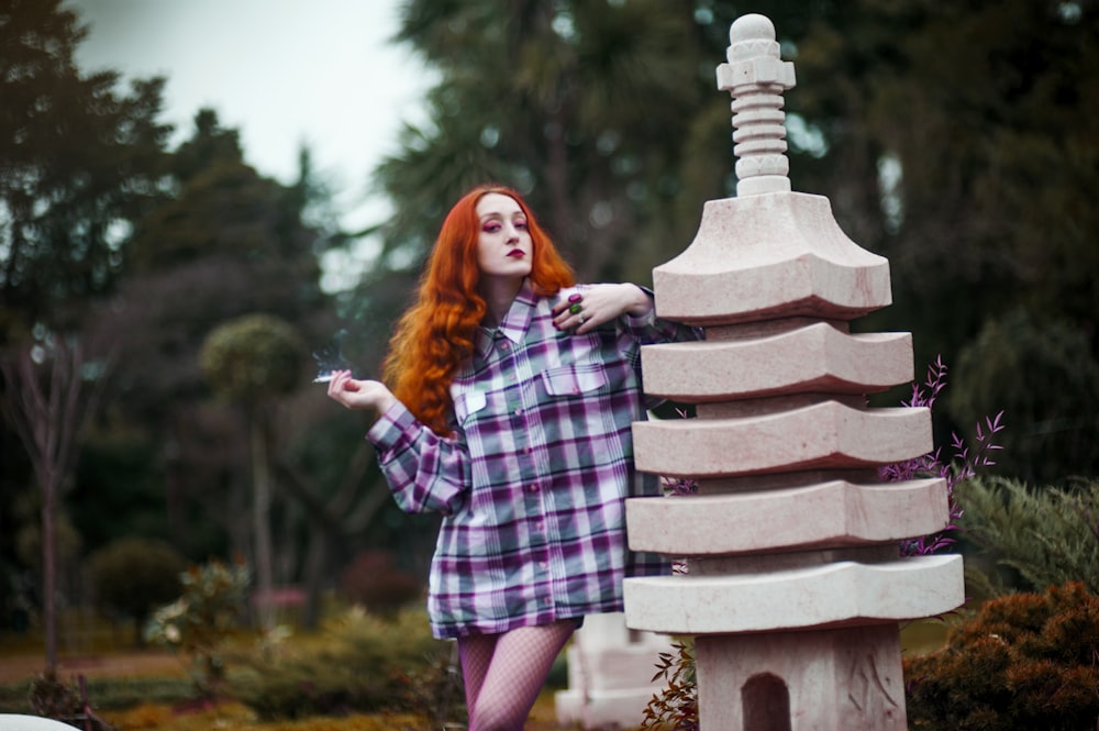 woman using cigarette while leaning on statue