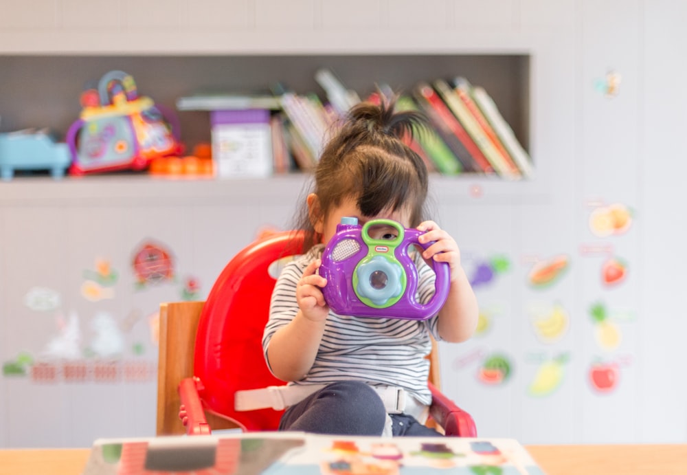 menina segurando roxo e verde brinquedo da câmera