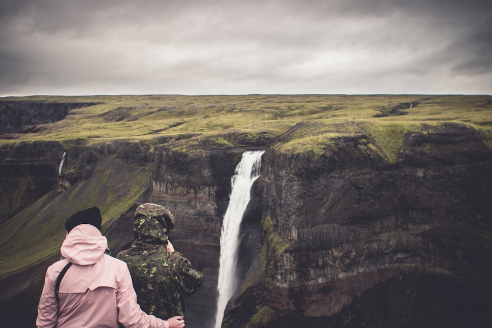 two person standing near the cliff watching the waterfalls