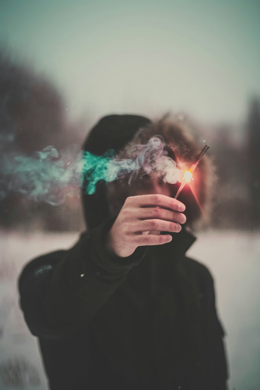 photo of person wearing hooded jacket holding lighted incense