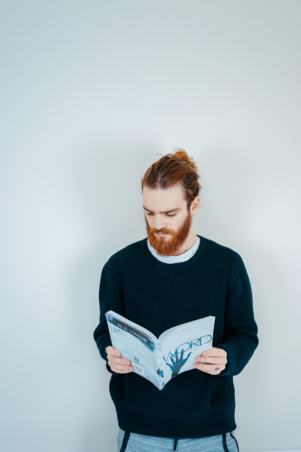 man reading book beside white wall