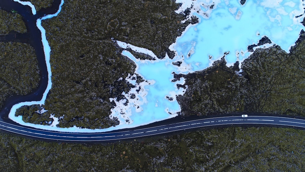 aerial view photo of vehicle crossing asphalt road between green trees near body of water