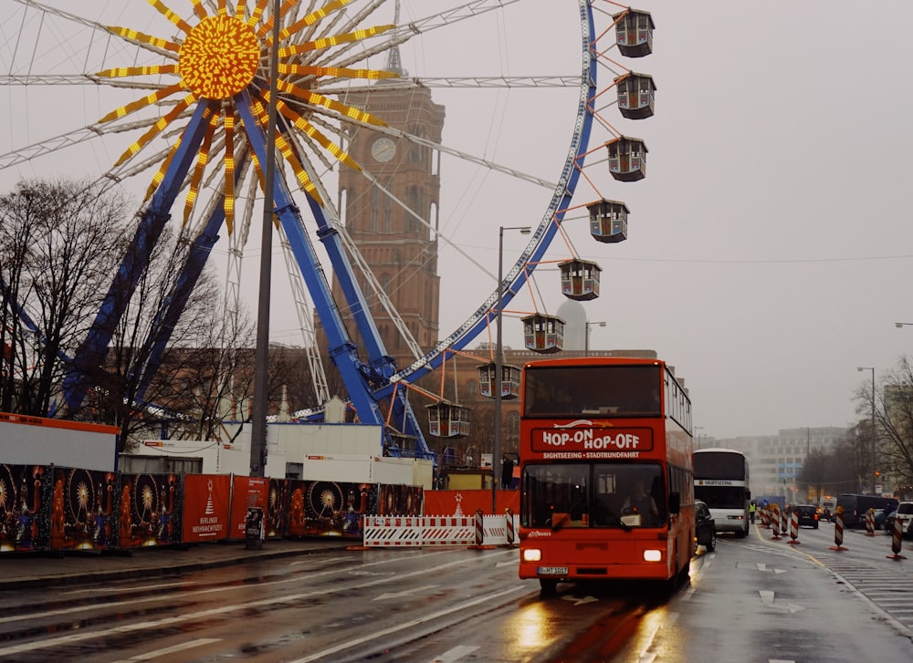 Bus rouge sur une route goudronnée près de la grande roue blanche et bleue