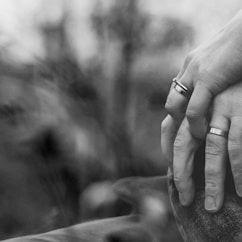 grayscale photo of two person holding hands with wedding rings