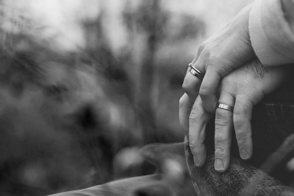 foto em tons de cinza de duas pessoas de mãos dadas com alianças de casamento