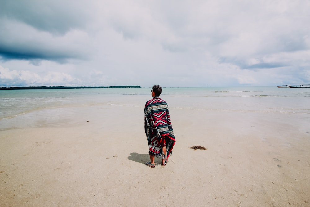 man wearing red and green scarf facing body of water