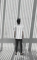 Model wearing a slmzone t-shirt and cap, standing against a textured concrete wall in soft natural light.