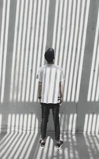 Model wearing a slmzone t-shirt and cap, standing against a textured concrete wall in soft natural light.