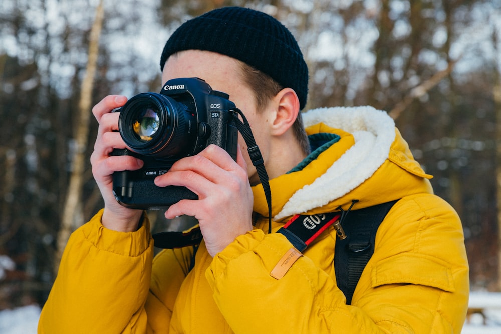 A man in a yellow coat and black hat with a camera in his hands