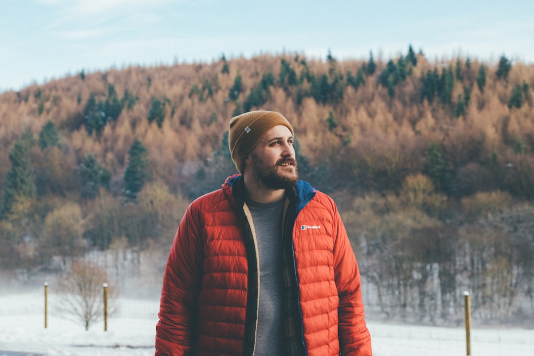 man wearing orange bubble jacket standing on snowfield staring at top-left side