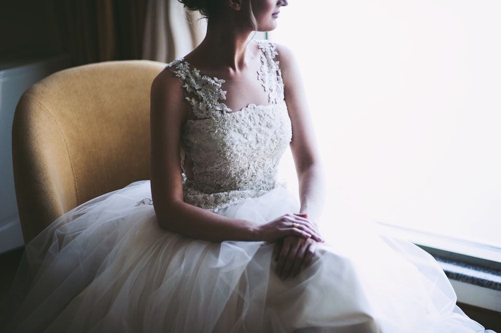 mujer en vestido de novia blanco sentado cerca de la ventana