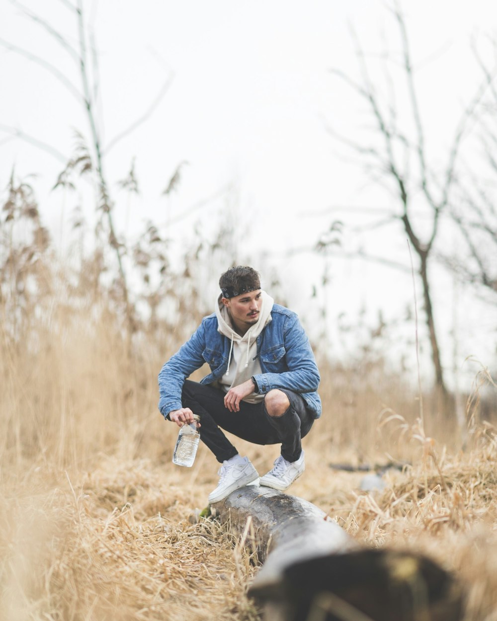 man in blue denim jacket sitting on wood log