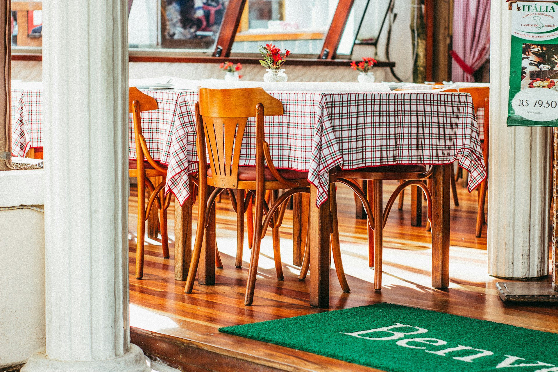 A warm, inviting shot of the rustic wooden dining tables in Vai da Carlo, adorned with red and green checkered tablecloths under soft Mediterranean lighting.