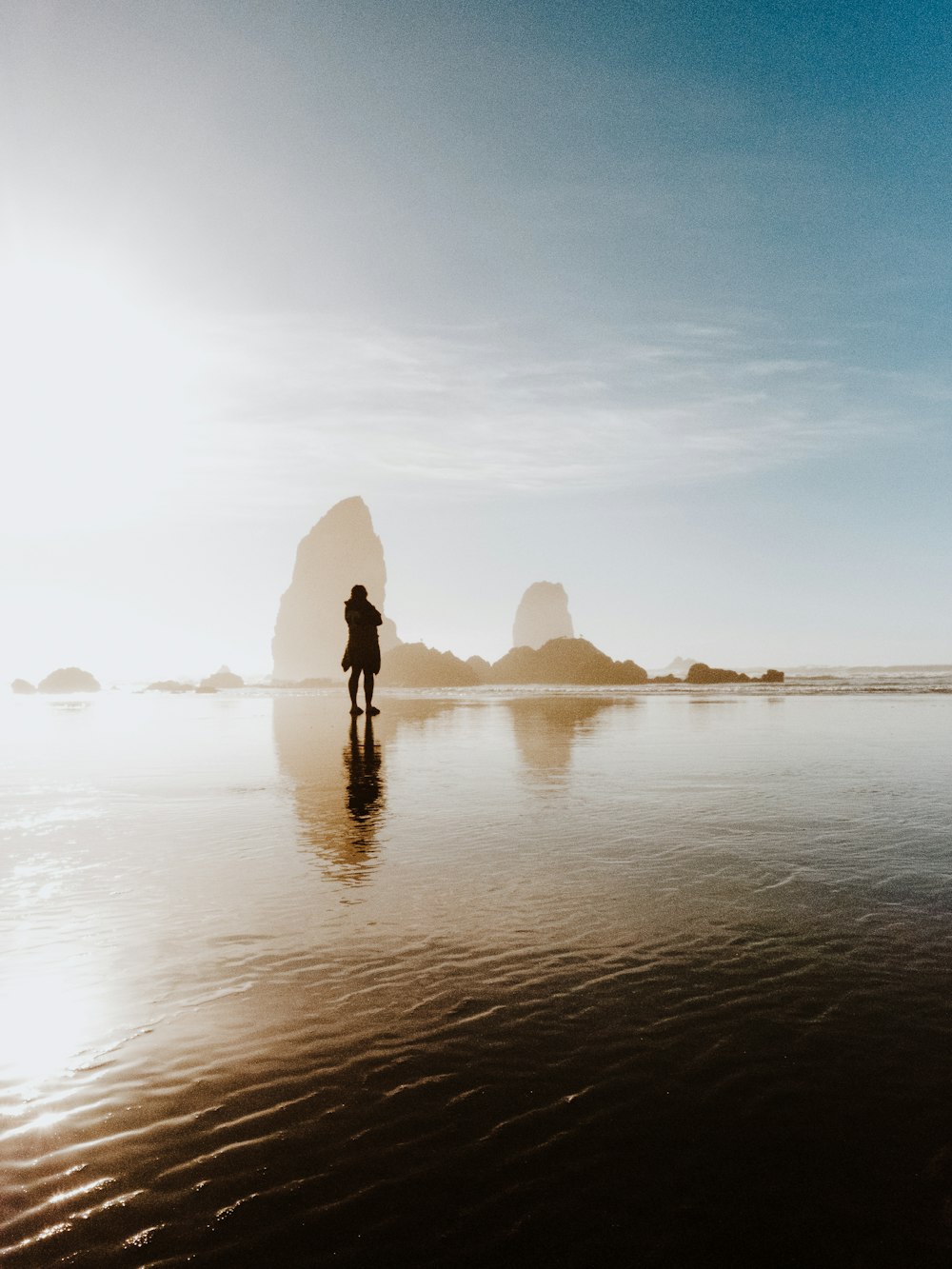 person standing in shallow body of water near boulders