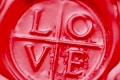 A close-up view of a red wax seal with the word 'LOVE' embossed in the center, divided into quadrants by lines.
