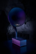 A modern, sleek phonograph-like speaker with a large, horn-shaped top emerging from a wooden base. The lighting casts a gradient of purples and blues, creating a futuristic and elegant appearance.
