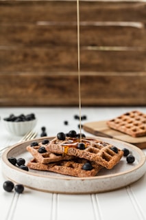 A plate of golden waffles topped with fresh berries and syrup on a rustic wooden table