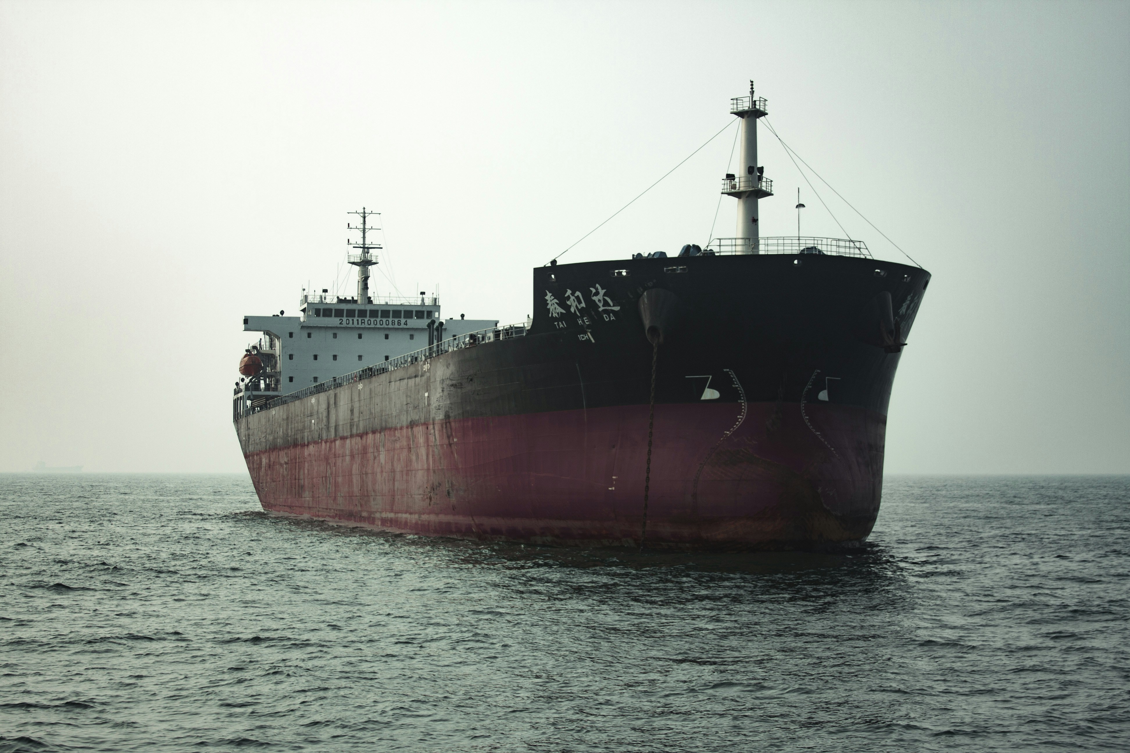 Large maritime cargo vessel with red hull sailing through calm blue waters representing global shipping operations