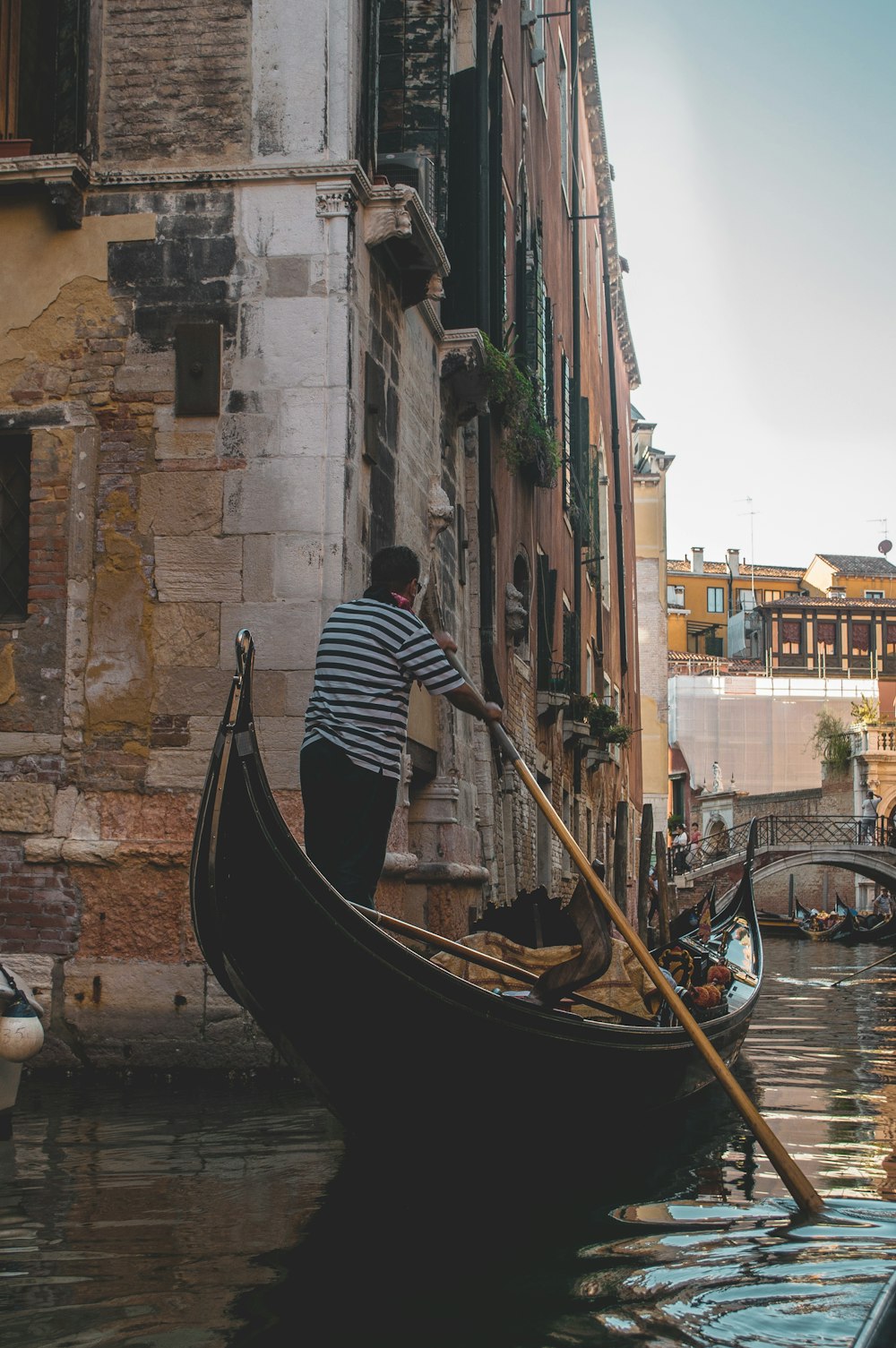 man paddling boat on canal under blue sky during daytime