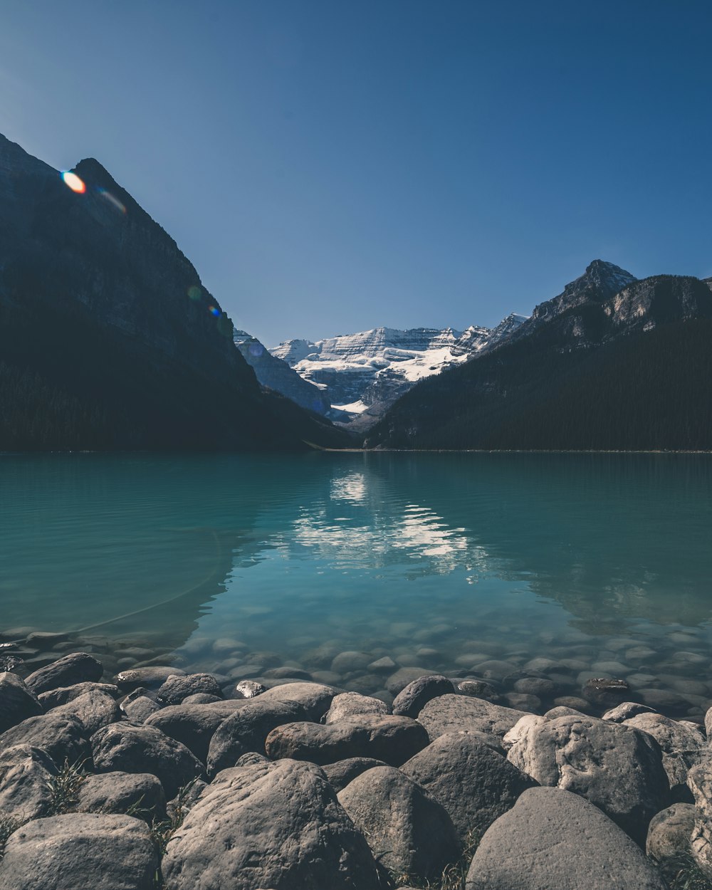 snow-covered mountain beside lake under blue sky during daytime