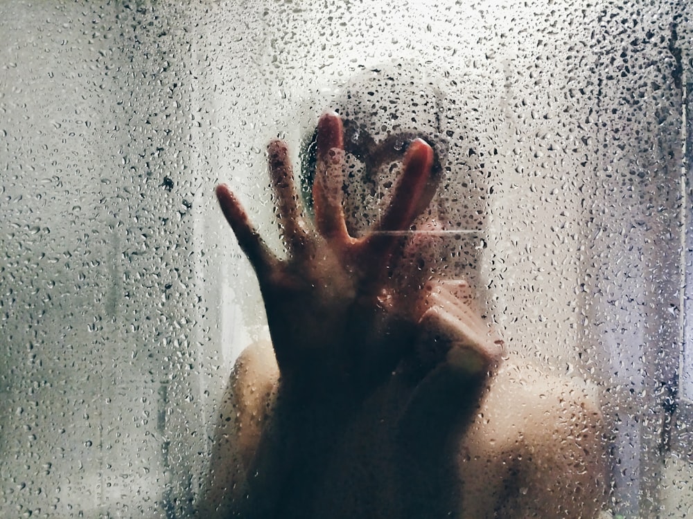 透明なシャワーガラスに触れる人
