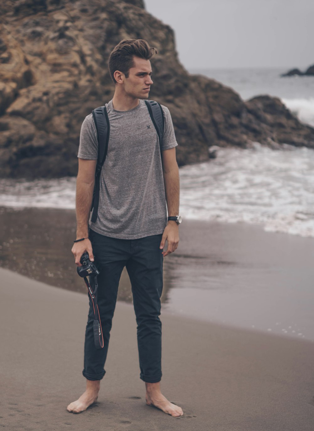 homme tenant un appareil photo reflex numérique sur le bord de la mer près d’un gros rocher
