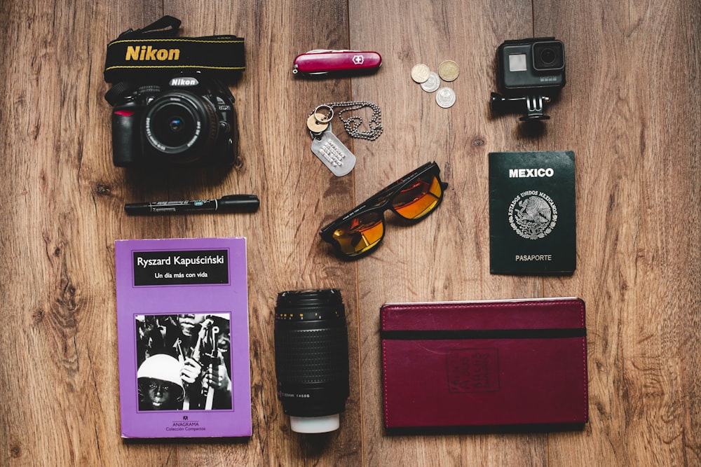 uma mesa coberta com uma máquina fotográfica, passaporte, óculos de sol e outros itens