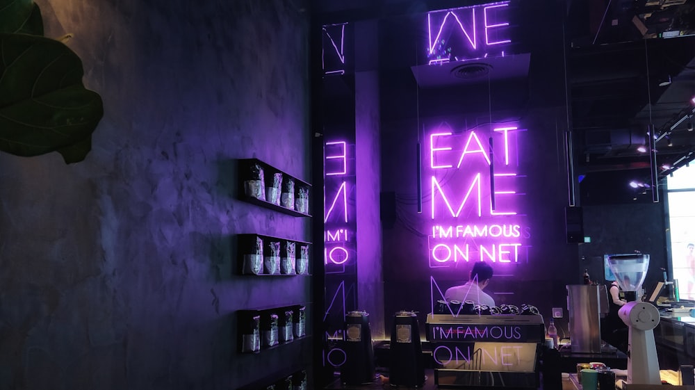 persona sentada frente a la señalización LED púrpura Eat Me I'm Famous On Net