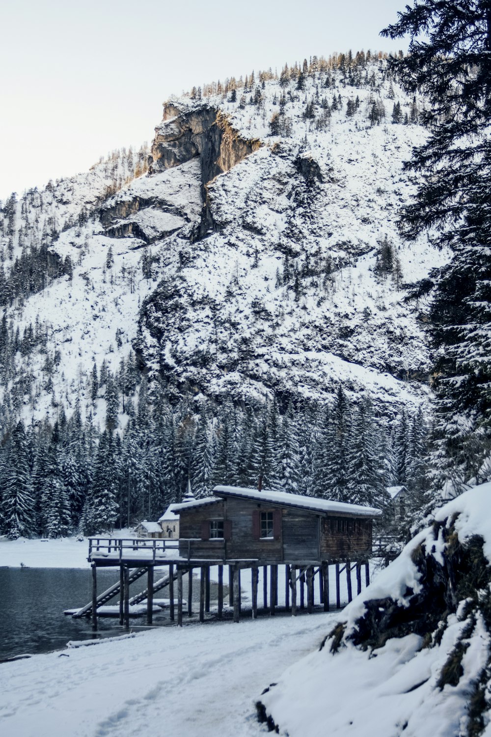 braunes Holzhaus neben einem Gewässer in der Nähe eines schneebedeckten Berges