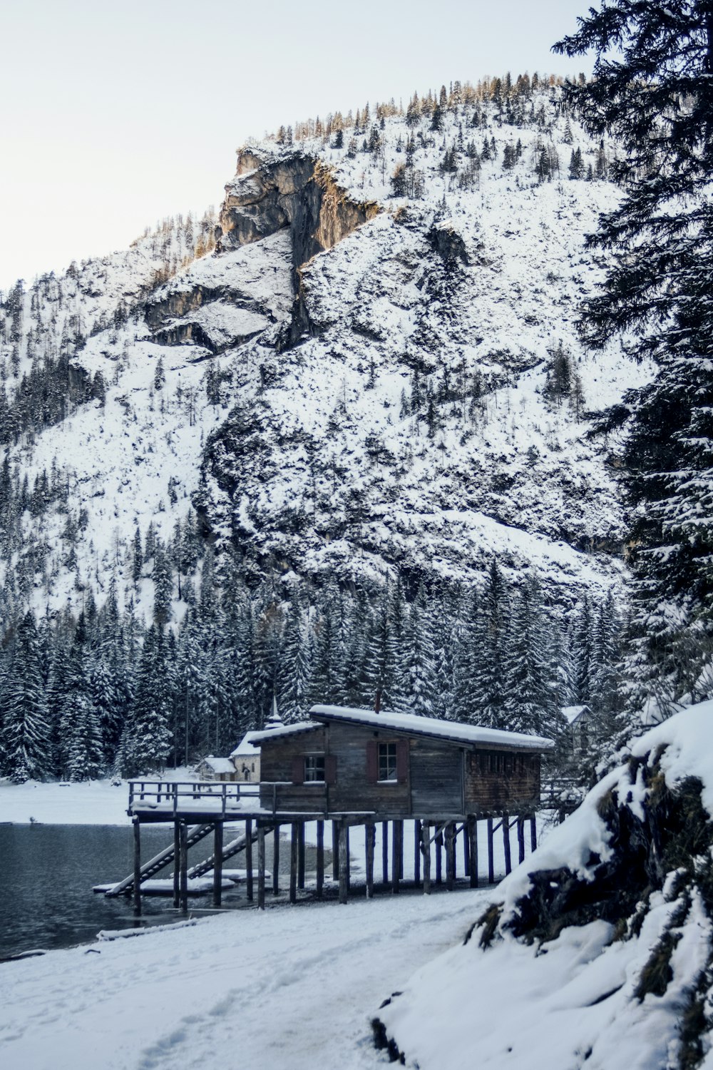 brown wooden house beside body of water near mountain covered by snow