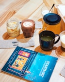 A steaming cup of rich hot chocolate with a swirl of cream, set beside a glass of refreshing lemonade on a craft services table.