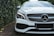 A luxury car with a sleek design, featuring a prominent grille and distinctive headlight. The vehicle is parked on a brick driveway, surrounded by lush greenery on one side.