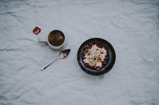 white ceramic mug filled with brown liquid beside stainless steel spoon