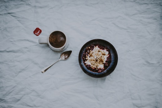 white ceramic mug filled with brown liquid beside stainless steel spoon